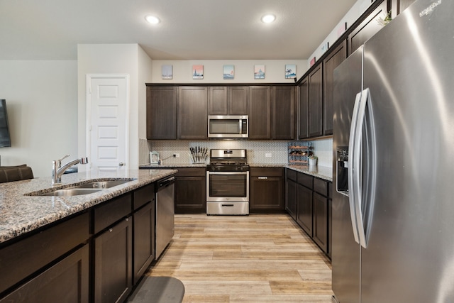 kitchen with light hardwood / wood-style floors, sink, light stone counters, appliances with stainless steel finishes, and tasteful backsplash