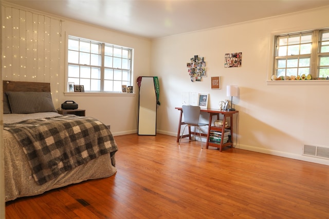 bedroom featuring ornamental molding, multiple windows, and light hardwood / wood-style floors