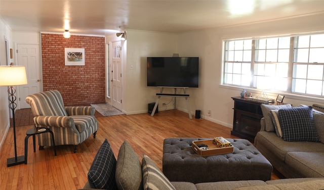 living room featuring light hardwood / wood-style flooring, brick wall, and crown molding