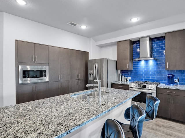 kitchen with light stone counters, light hardwood / wood-style flooring, sink, wall chimney range hood, and appliances with stainless steel finishes