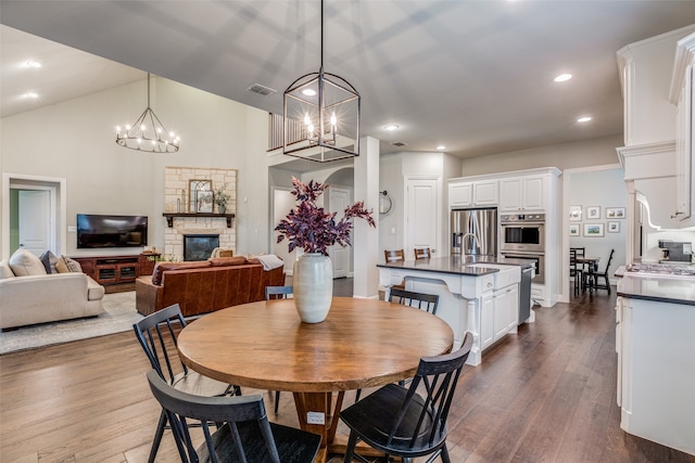 dining space with lofted ceiling, an inviting chandelier, sink, dark hardwood / wood-style floors, and a fireplace