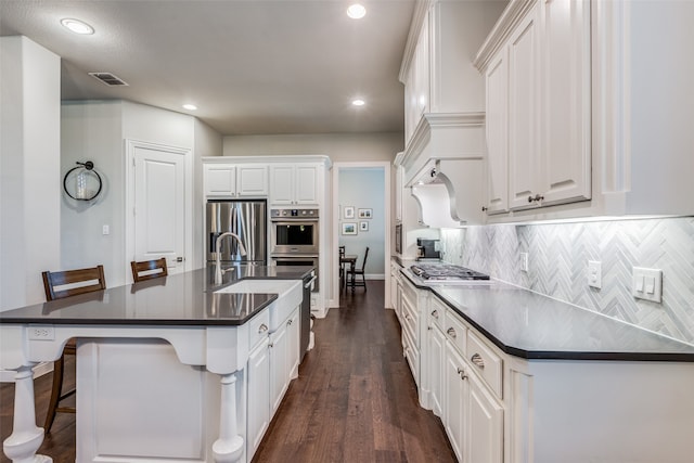 kitchen featuring a kitchen bar, appliances with stainless steel finishes, decorative backsplash, a kitchen island with sink, and white cabinetry