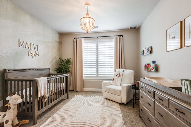 bedroom featuring a crib, light colored carpet, and an inviting chandelier