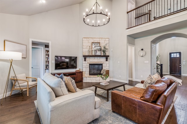 living room featuring a stone fireplace, dark hardwood / wood-style flooring, a high ceiling, and a notable chandelier