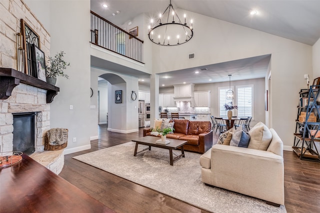 living room featuring a fireplace, a towering ceiling, dark hardwood / wood-style floors, and an inviting chandelier