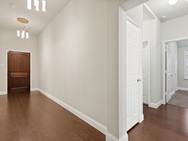 hall with dark wood-type flooring and a notable chandelier