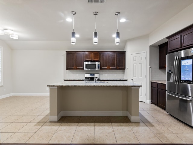 kitchen with stainless steel appliances, light stone countertops, an island with sink, and tasteful backsplash