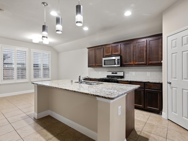 kitchen with a center island with sink, sink, light stone counters, decorative light fixtures, and gas range oven