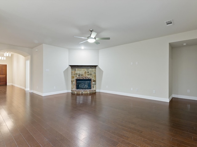 unfurnished living room with dark hardwood / wood-style flooring, a stone fireplace, and ceiling fan