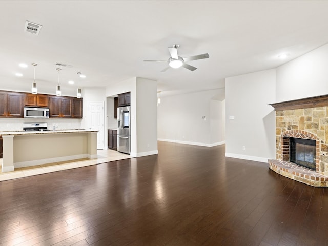 unfurnished living room featuring hardwood / wood-style floors, a stone fireplace, and ceiling fan