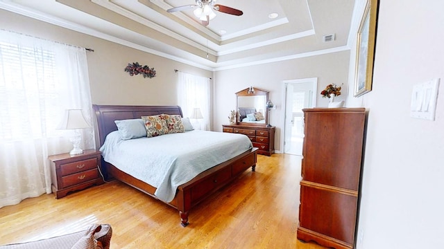 bedroom with crown molding, a raised ceiling, visible vents, ceiling fan, and light wood-type flooring