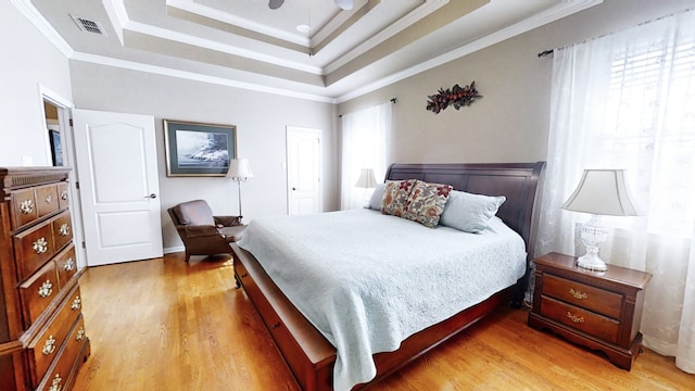 bedroom with crown molding, light wood finished floors, a raised ceiling, visible vents, and ceiling fan