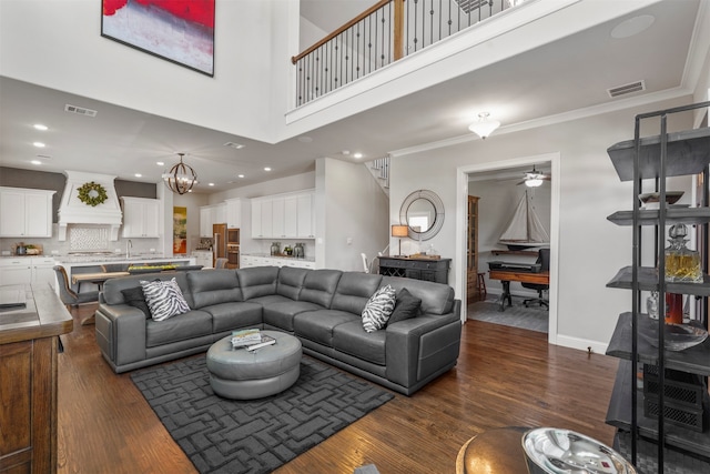 living room with dark wood-type flooring, ceiling fan with notable chandelier, a high ceiling, and crown molding