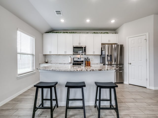 kitchen with stainless steel appliances, vaulted ceiling, an island with sink, backsplash, and white cabinetry