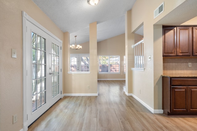 doorway to outside with an inviting chandelier, lofted ceiling, french doors, and light hardwood / wood-style flooring