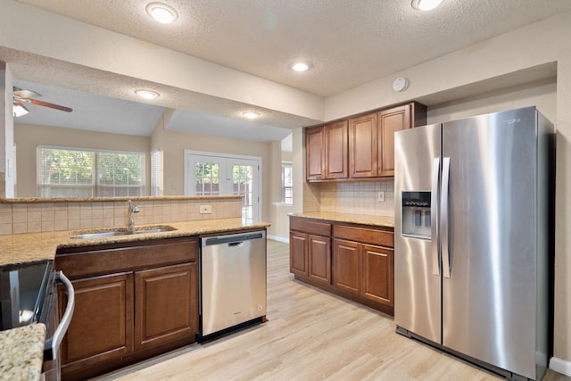 kitchen with stainless steel appliances, backsplash, a textured ceiling, sink, and light hardwood / wood-style flooring