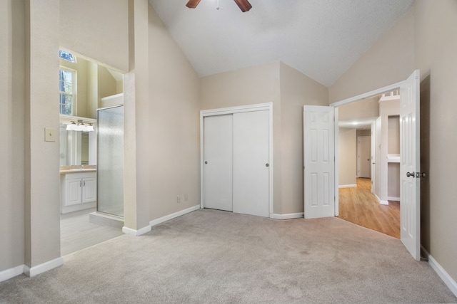 unfurnished bedroom with high vaulted ceiling, light colored carpet, ceiling fan, and ensuite bath