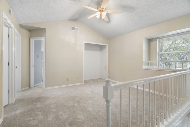 hall featuring a textured ceiling, lofted ceiling, and light carpet