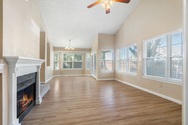 unfurnished living room with light wood-type flooring, ceiling fan with notable chandelier, and high vaulted ceiling