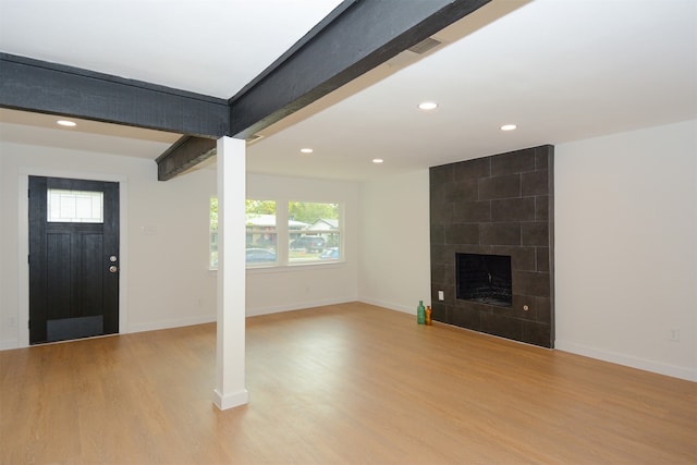 interior space featuring light wood-type flooring, beamed ceiling, and a tile fireplace