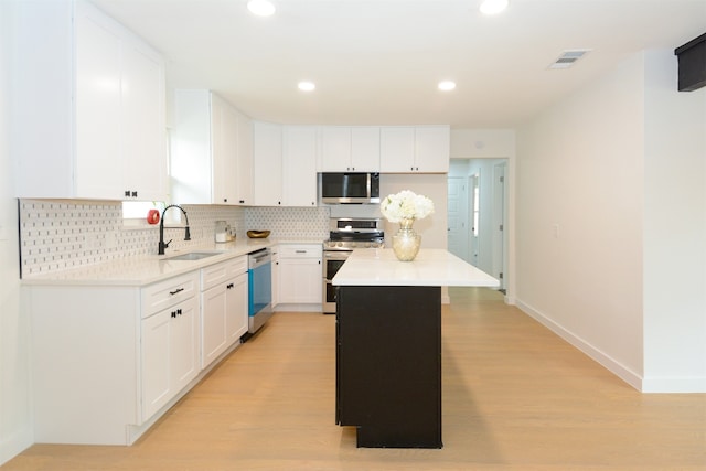 kitchen featuring appliances with stainless steel finishes, a center island, white cabinetry, sink, and light hardwood / wood-style flooring