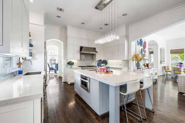 kitchen with sink, white cabinets, oven, wall chimney exhaust hood, and a center island