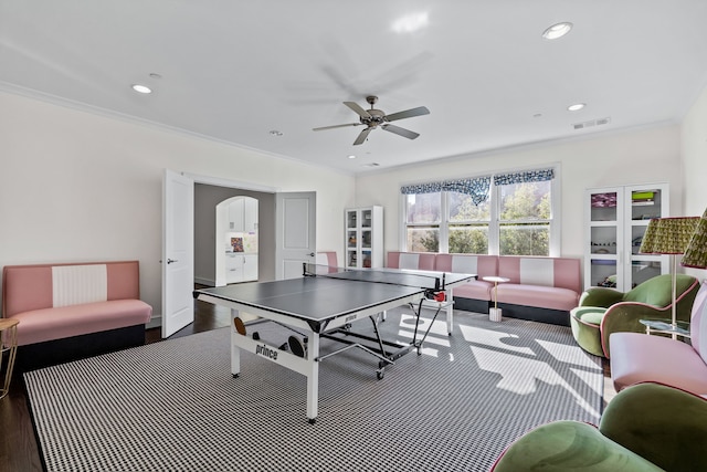 playroom with dark wood-type flooring, ornamental molding, and ceiling fan