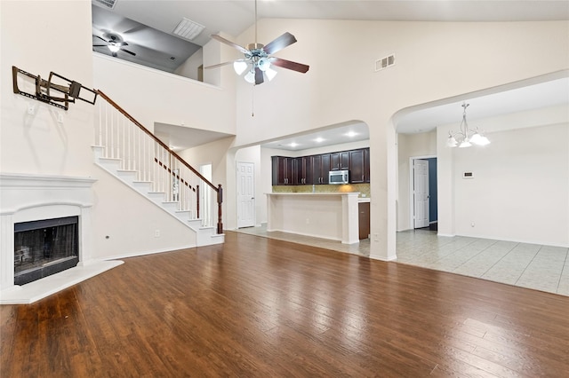 unfurnished living room featuring a fireplace with raised hearth, light wood-style flooring, ceiling fan with notable chandelier, and visible vents