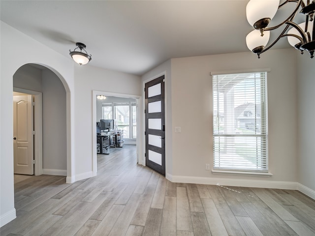 foyer with arched walkways, light wood-type flooring, and baseboards