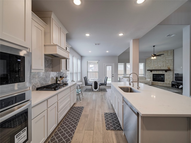 kitchen with white cabinetry, light wood-type flooring, stainless steel appliances, and an island with sink