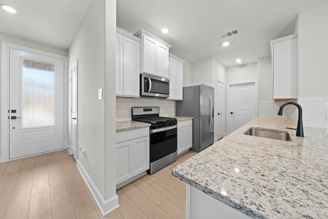 kitchen with white cabinetry, sink, light stone counters, and appliances with stainless steel finishes