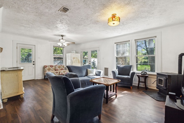 living room featuring a wood stove, dark hardwood / wood-style flooring, a textured ceiling, and ceiling fan