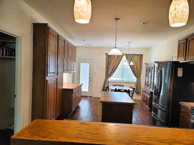 kitchen featuring dark wood-type flooring, a kitchen island, black refrigerator with ice dispenser, and decorative light fixtures