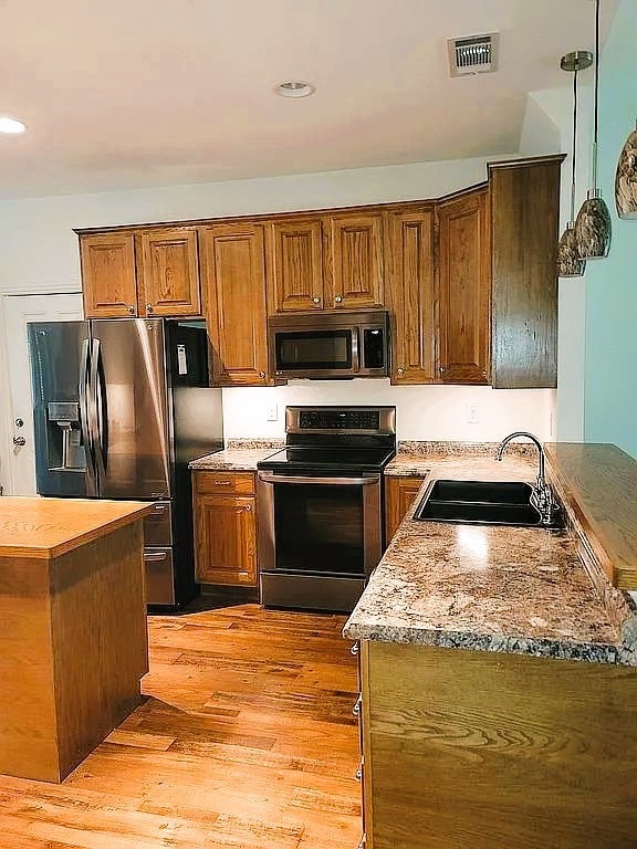 kitchen with stainless steel appliances, sink, light stone counters, hanging light fixtures, and light wood-type flooring