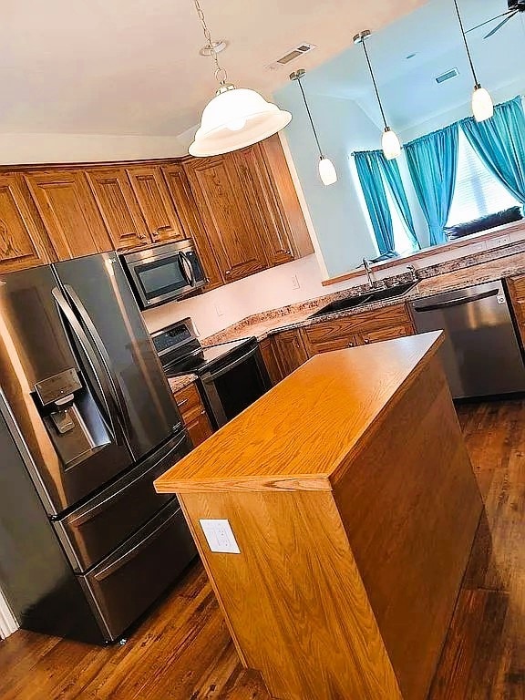 kitchen featuring pendant lighting, appliances with stainless steel finishes, vaulted ceiling, and dark hardwood / wood-style floors