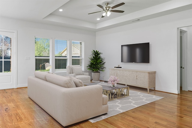 living room featuring ceiling fan, light hardwood / wood-style floors, and a raised ceiling