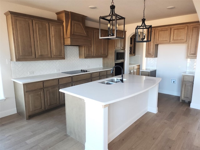 kitchen with custom range hood, sink, a notable chandelier, hardwood / wood-style floors, and an island with sink