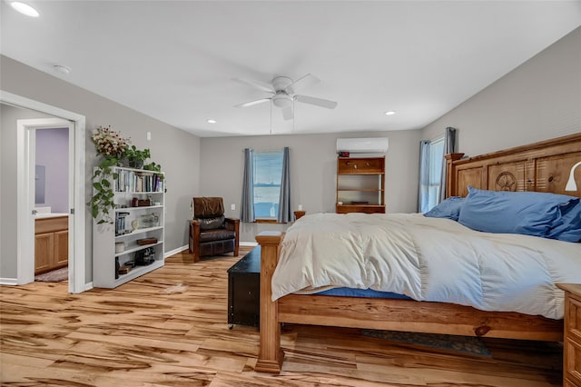 bedroom with ceiling fan, connected bathroom, an AC wall unit, and light wood-type flooring