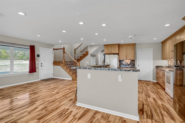 kitchen with dark stone countertops, backsplash, white appliances, and light hardwood / wood-style floors