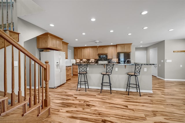 kitchen featuring ceiling fan, a breakfast bar area, white refrigerator with ice dispenser, stainless steel fridge, and light wood-type flooring