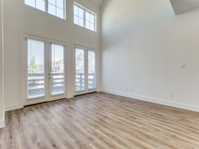 empty room with light wood-type flooring and a towering ceiling