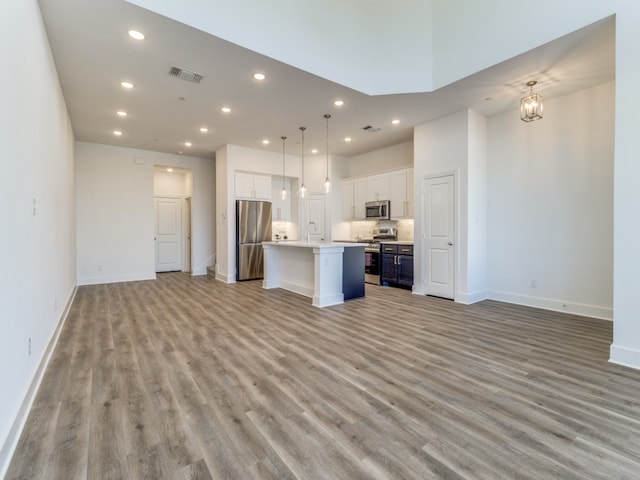 kitchen featuring a kitchen island with sink, appliances with stainless steel finishes, white cabinetry, and decorative light fixtures