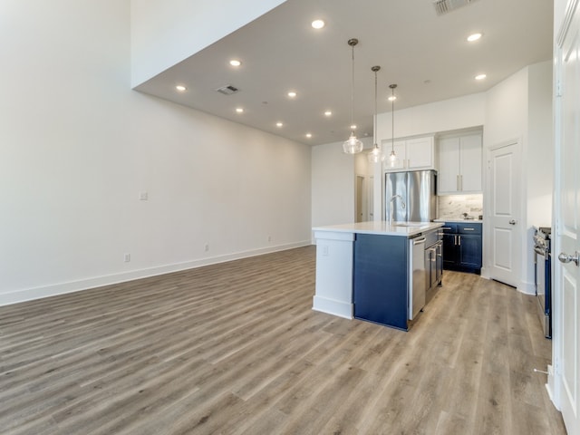 kitchen featuring white cabinetry, appliances with stainless steel finishes, hanging light fixtures, an island with sink, and light hardwood / wood-style flooring