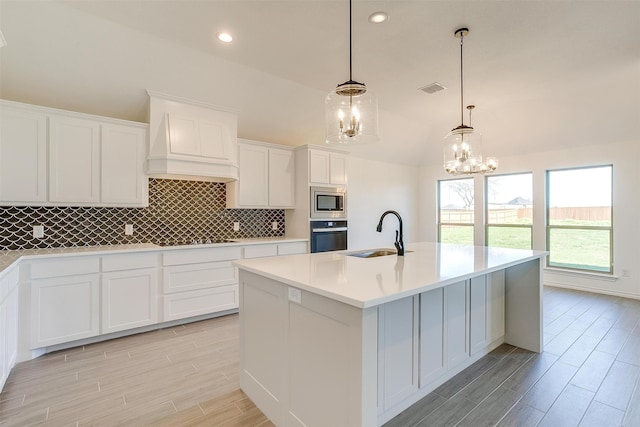 kitchen featuring stainless steel appliances, sink, a kitchen island with sink, a notable chandelier, and premium range hood