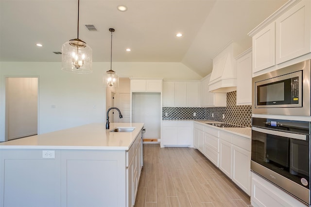 kitchen with sink, appliances with stainless steel finishes, a kitchen island with sink, white cabinets, and pendant lighting