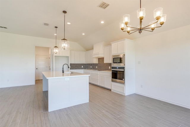 kitchen featuring stainless steel appliances, white cabinets, sink, an island with sink, and pendant lighting