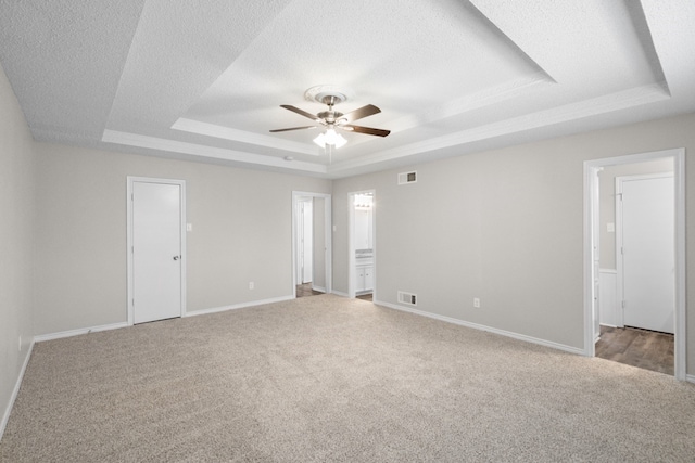 carpeted empty room featuring a textured ceiling, ceiling fan, and a raised ceiling