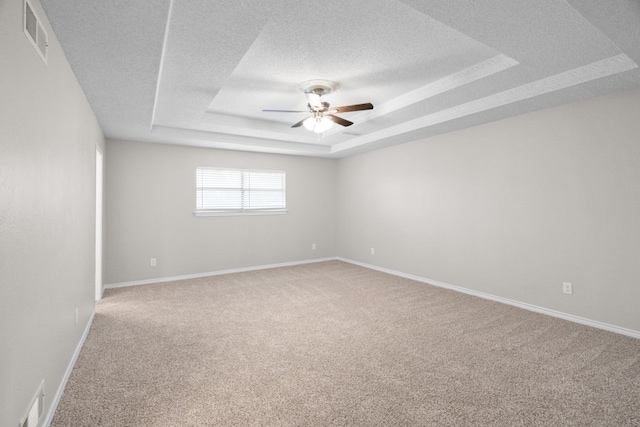 empty room with carpet, ceiling fan, and a tray ceiling