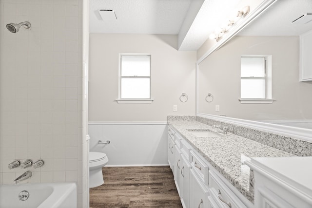 full bathroom with vanity, a textured ceiling, tiled shower / bath combo, hardwood / wood-style flooring, and toilet