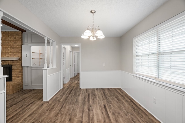 unfurnished dining area featuring a textured ceiling, a fireplace, dark hardwood / wood-style floors, and a chandelier